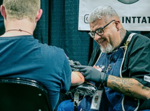 Laughing tattoo artist working on a customer.