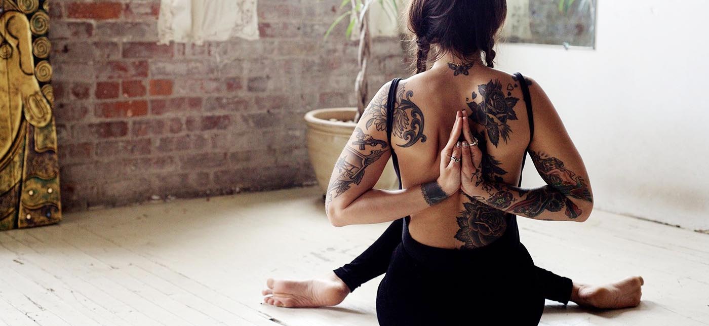 Women with back tattoo doing a yoga pose.