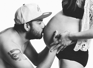 Tattooed man kissing a pregnant belly.
