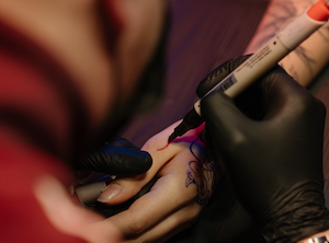 Close-up of an artist's hand drawing a design on skin.